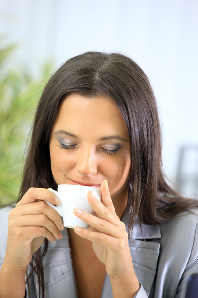 Portrait of relaxed businesswoman holding a cup of coffee in her office at - Photo, Image