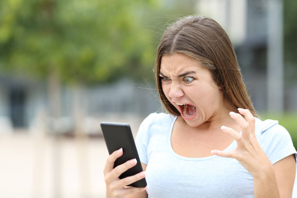 Angry teen watching media on smartphone in a park - Foto, afbeelding