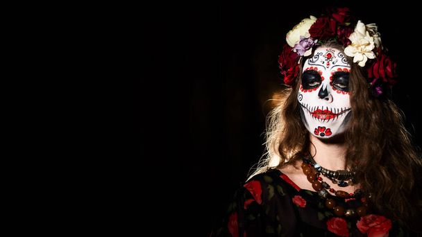 Woman in santa muerte makeup on a black background. Girl wearing traditional mexican holy death costume for halloween. Copy space - Photo, Image