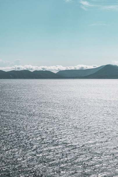 Μπλε Ιόνιο πέλαγος θέα στο νησί της Λευκάδας. Φωτεινή μέρα με χαμηλά σύννεφα πάνω από μακρινά νησιά. Κατακόρυφο χρώμα θαλασσινό φόντο - Φωτογραφία, εικόνα