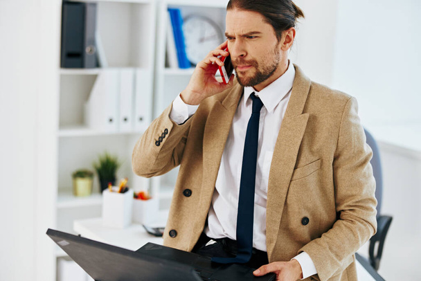 hombre en chaqueta beige sosteniendo un teléfono portátil tecnologías de oficina - Foto, imagen