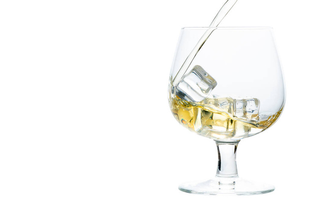 wlać whisky lub brandy na kostkę lodu w szklance Snifter lub Balon izolowane na białym tle, koncepcja napojów - Zdjęcie, obraz