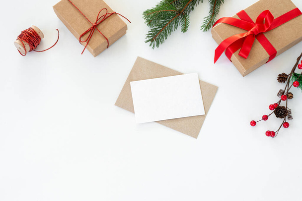 Рождественская композиция Карточка поздравления, макет конверта. Украшение рождественскими подарками с красным луком, красными ягодами, лентой, елками и шишками на белом фоне. - Фото, изображение