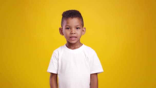 Shh, its secret. Cute african american boy putting finger on lips, showing privacy gesture to camera, orange background - Footage, Video