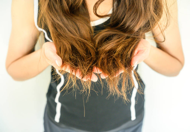 Zugeschnittene Ansicht der Frau, die ihr beschädigtes gespaltenes Haar hält (Fokus an den Haarenden). Haarschäden sind ein Risiko für weitere Schäden und Brüche. Es kann auch langweilig oder krauses Aussehen haben und schwierig zu handhaben sein. - Foto, Bild