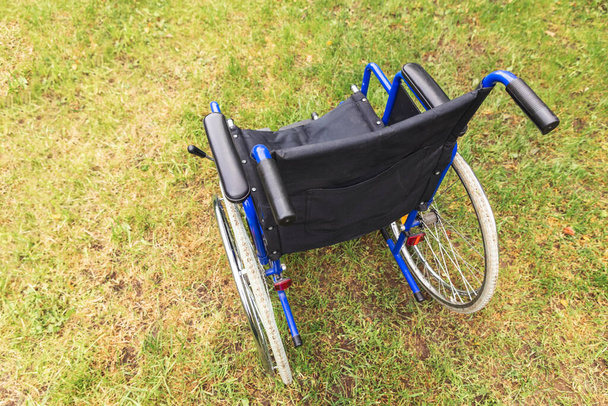 Empty wheelchair standing on grass in hospital park waiting for patient services. Invalid chair for disabled people parked outdoor in nature. Handicap accessible symbol. Health care medical concept - Фото, изображение