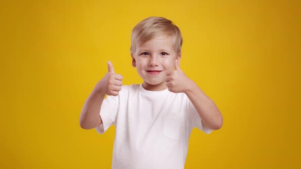 Die Zustimmung der Kinder. Studioporträt des niedlichen kleinen kaukasischen Jungen, der mit beiden Händen Daumen nach oben streckt und in die Kamera lächelt - Filmmaterial, Video