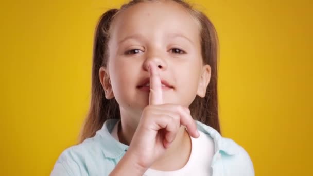 Schweigt. Lustiges kleines Mädchen zeigt shh Zeichen, hält den Finger auf den Lippen und schaut in die Kamera, orangefarbener Studiohintergrund - Filmmaterial, Video