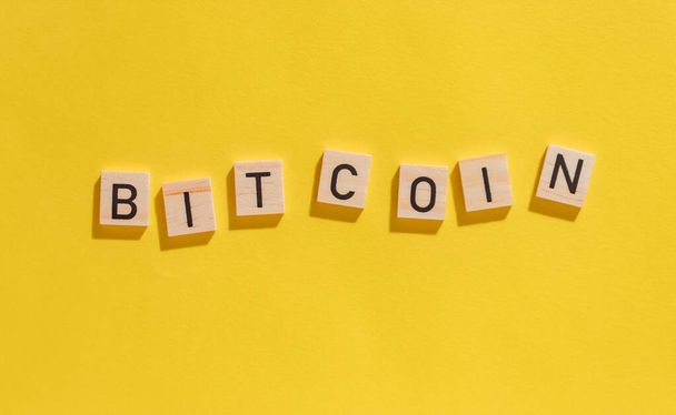 Bitcoin felirat fa betűkkel sárga alapon kemény árnyékokkal felülnézet - Fotó, kép