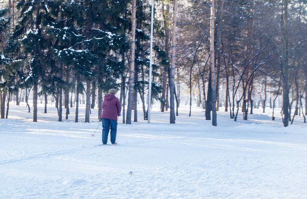 Uma mulher idosa de casaco esquiando em um parque de inverno, vista pelas costas. - Foto, Imagem