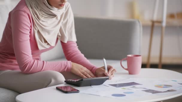 Tuntematon musliminainen työskentelee kotona, laskee taloutta ja tekee muistiinpanoja, tekee liiketoimintasuunnitelman, vapaa tila - Materiaali, video