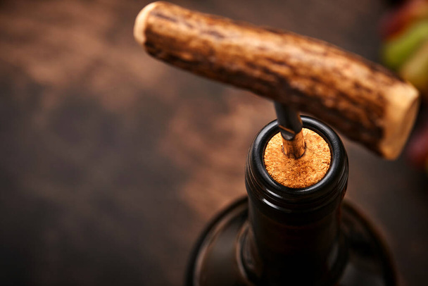 Bottle wine with corkscrew. Opening a wine bottle with a corkscrew in a restaurant. Wine composition on dark rustic background with copy space. Mock up. - Photo, Image