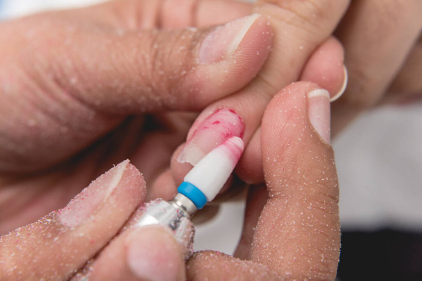 Een manicure gebruikt een elektrisch nagelvijl om nagellak en de resten van het acryl te verwijderen. Nagelverlenging verwijderen in een salon of salon. - Foto, afbeelding