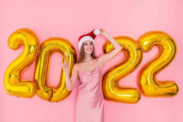 Smiling adult girl hold glass of champagne in Santas hat 2022 golden air balloons New Year concept  - Zdjęcie, obraz