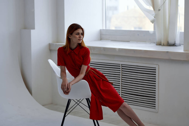 Şık bir sandalyede poz veren kırmızı elbiseli güzel bir kadın. - Fotoğraf, Görsel