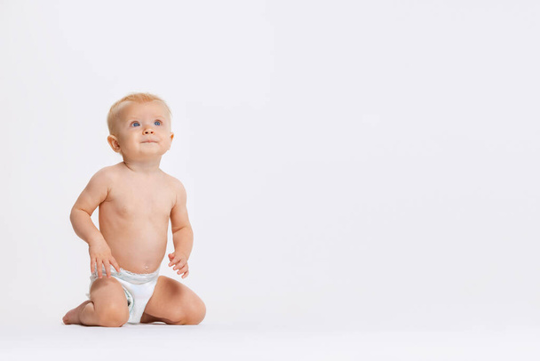 Portrait complet de petite fille tout-petit mignonne, bébé assis calmement dans une couche isolée sur fond de studio blanc - Photo, image