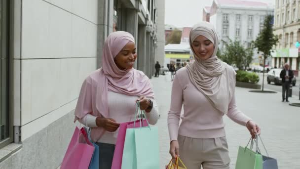 Zwarte vrijdag verkoop. Twee vrolijke moslimvrouwen lopen met veel boodschappentassen en lachen, genieten van herfstshoppen - Video