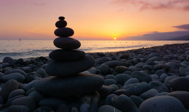 Montón de piedras grises zen en la playa al atardecer, hermoso paisaje marino. Hecho de torre de piedra como concepto de vacaciones de equilibrio de descanso. - Foto, Imagen
