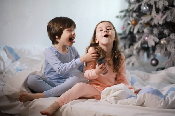 Rodzina z dziećmi bawiącymi się na łóżku pod kołdrą podczas świąt Bożego Narodzenia. - Zdjęcie, obraz