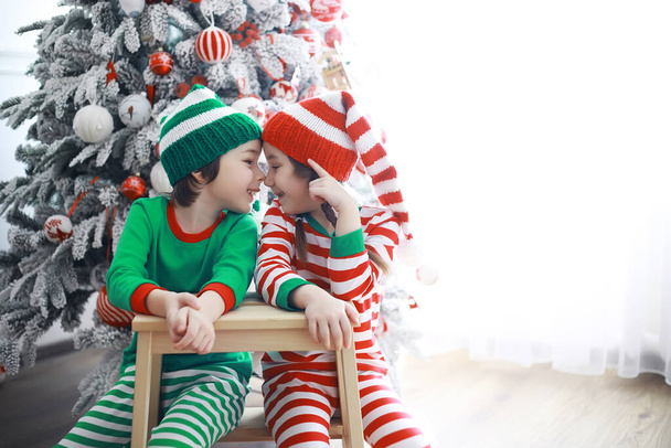Des enfants mignons en costumes d'elfe de Noël dans une chambre joliment décorée pour Noël. Le temps des miracles. Cadeaux du Père Noël - Photo, image