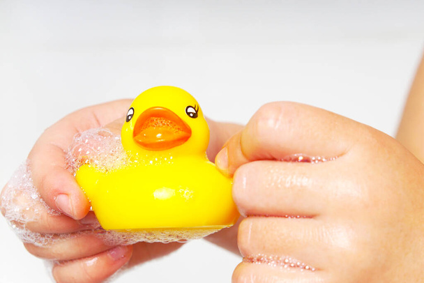 Cute yellow duck in children's wet hands. The child shows care for a small toy. Water games. The bathroom is a place for games. - Zdjęcie, obraz
