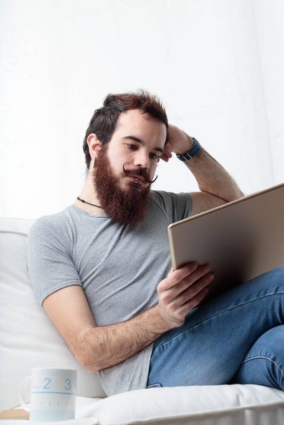 homem com barba e bigode lê a partir da tela de um grande tablet digital, estuda, trabalha ou gosta do entretenimento que prefere - Foto, Imagem