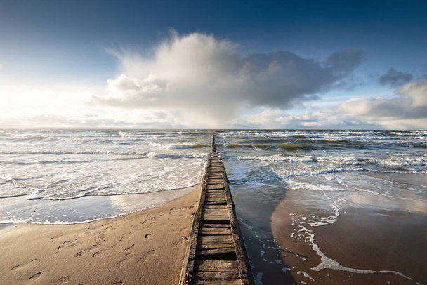 Kilátás a Balti-tengerre a homokos partról (homokdűnék). Tiszta ég, ragyogó felhők, napsugarak. Hullámok, víz fröccsen. Régi móló (móló) halászhajók számára. Idilli tengerpart. Tél, éghajlat, természet. Dánia - Fotó, kép