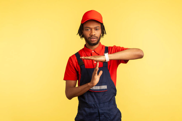 Serious worker wearing uniform, showing time out gesture, need break, working in service industry, courier delivery, housekeeping maintenance. Indoor studio shot isolated on yellow background. - Zdjęcie, obraz