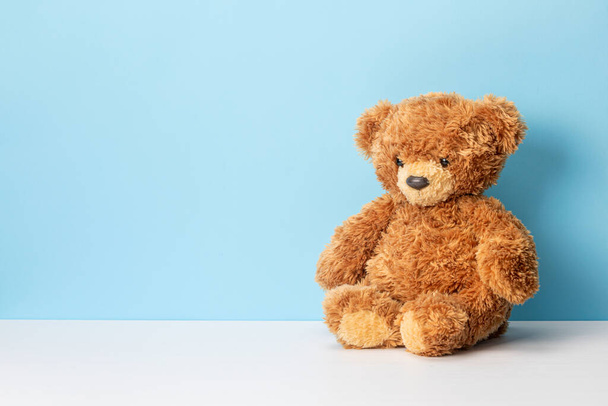Teddy bear sits on a white table and blue background. Template Copy space for text. - 写真・画像