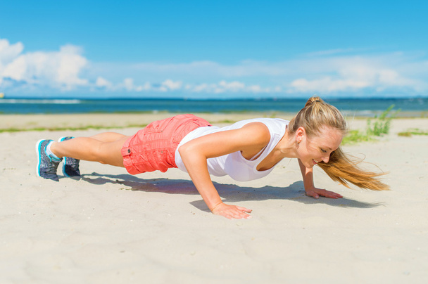 vrouw doen push-ups op het strand. - Foto, afbeelding
