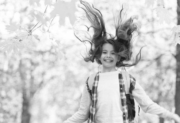 Happy energetic kid with long brunette hair jump in autumn park back to school season, salon - Foto, imagen