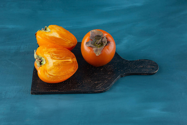 Whole and half sliced persimmon fruits on black cutting board.  - Valokuva, kuva