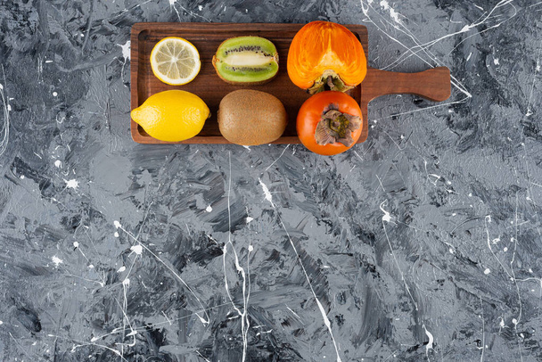 Houten bord met hele en gesneden verse vruchten op marmer  - Foto, afbeelding