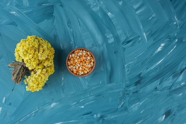 Pişmemiş mısır tohumlarıyla dolu bir kase ve bir buket çiçek.  - Fotoğraf, Görsel