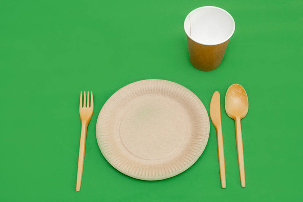 Recyclable fork, spoon, knife, plate and cup on a green background. Kitchen utensils. Top view. Minimalist Style. Copy space. - Zdjęcie, obraz