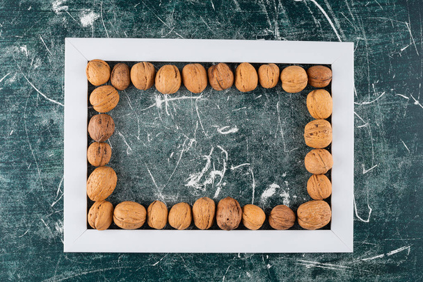 Pile of shelled walnuts with empty frame on marble background  - Fotografie, Obrázek