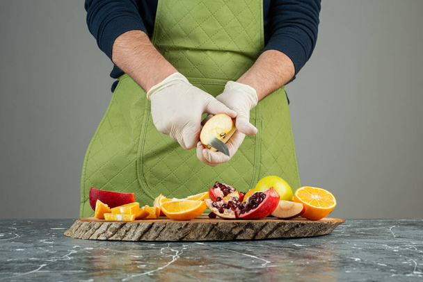 Male hand in gloves cutting fresh apple on marble table - Photo, Image