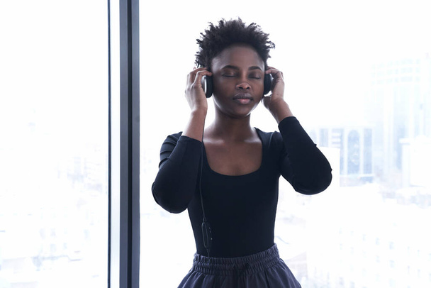 Una donna afroamericana ascolta musica con le cuffie. Una giovane donna in uniforme sportiva sullo sfondo di una finestra - Foto, immagini