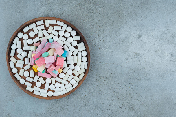 Wooden plate of many chewing gums on stone surface.  - Photo, image