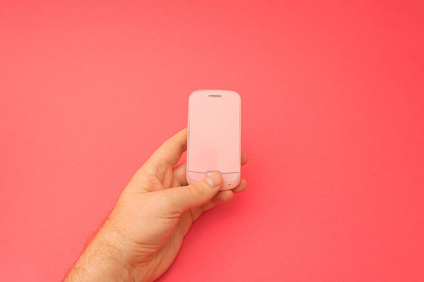 Hand hält rosa 3D-Smartphone vor rotem Hintergrund. 3D-Illustration Design-Vorlage Hintergrund. Top-Handy-Nachricht. Werbeidee. Leerer Kopierraum - Foto, Bild