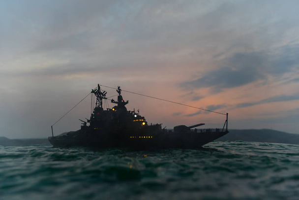 Σχέδιο πολέμου. Σκηνή νυχτερινής μάχης στη θάλασσα. Δραματική επίδραση τονισμένων νεφών. Η σιλουέτα του πολεμικού πλοίου το ηλιοβασίλεμα. Μικρογραφία δημιουργική διακόσμηση τραπέζι. Επιλεκτική εστίαση - Φωτογραφία, εικόνα