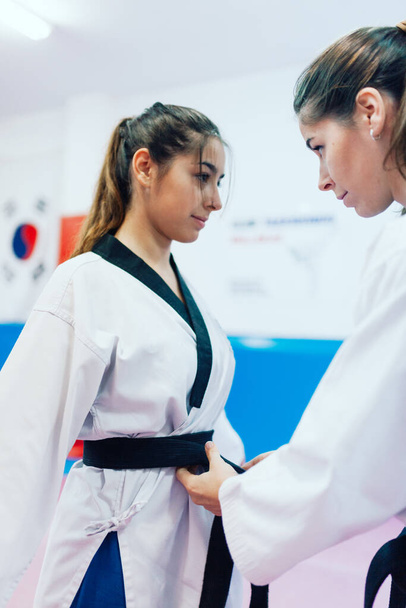 Két fiatal nő öltözteti egymást a taekwondo kimonójukba. - Fotó, kép