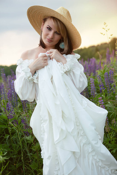 Beautiful young woman in a field of blooming lupines on a warm summer day - Foto, immagini