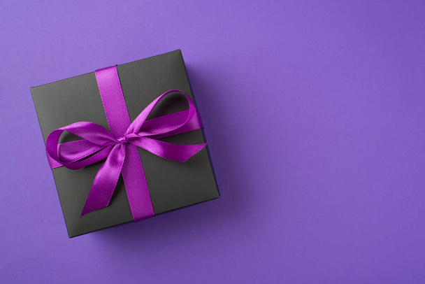 Photo ci-dessus de boîte cadeau noire avec ruban enveloppé comme arc isolé sur le fond violet - Photo, image