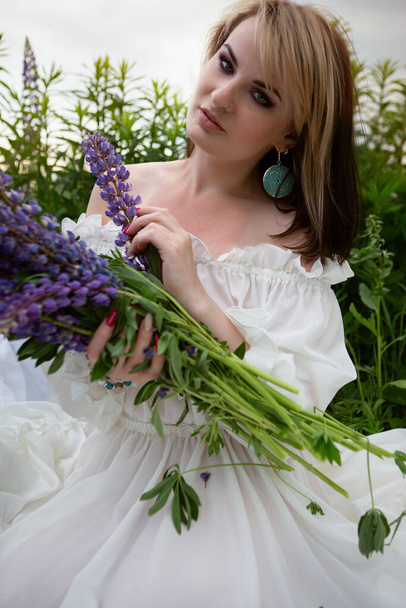 Beautiful young woman in a field of blooming lupines on a warm summer day - Foto, afbeelding