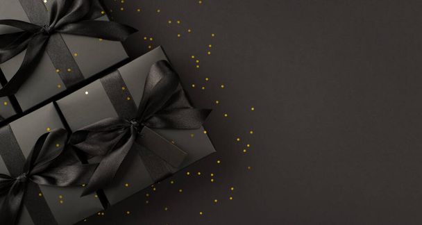 Top view photo of black gift boxes with black ribbon bow tag and golden confetti on isolated black background with blank space - Valokuva, kuva