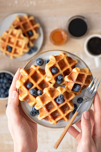 Waffles with blueberries in female hands, top view. Sweet food - Foto, Imagen