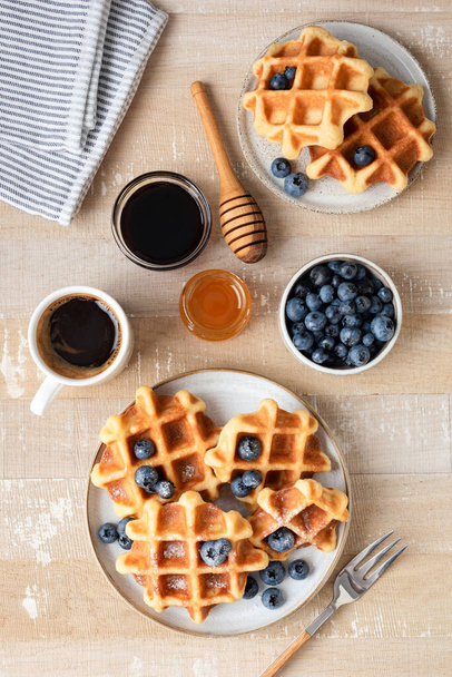 Sweet waffles with blueberries, coffee and honey on a wooden table background. Table top view. Breakfast or brunch food - Fotó, kép
