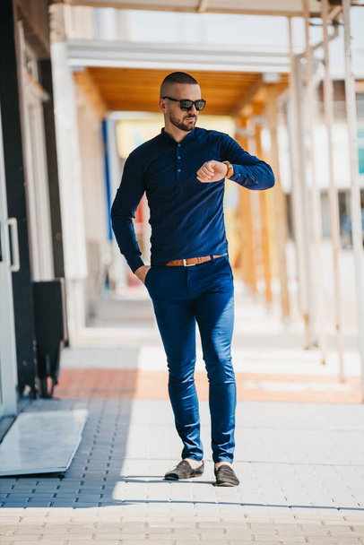 A cool handsome Caucasian man wearing an elegant blue shirt and sunglasses posing outdoor - Foto, immagini