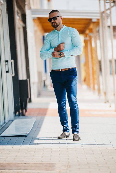 A cool handsome Caucasian man wearing an elegant light blue shirt and sunglasses posing outdoor - Valokuva, kuva